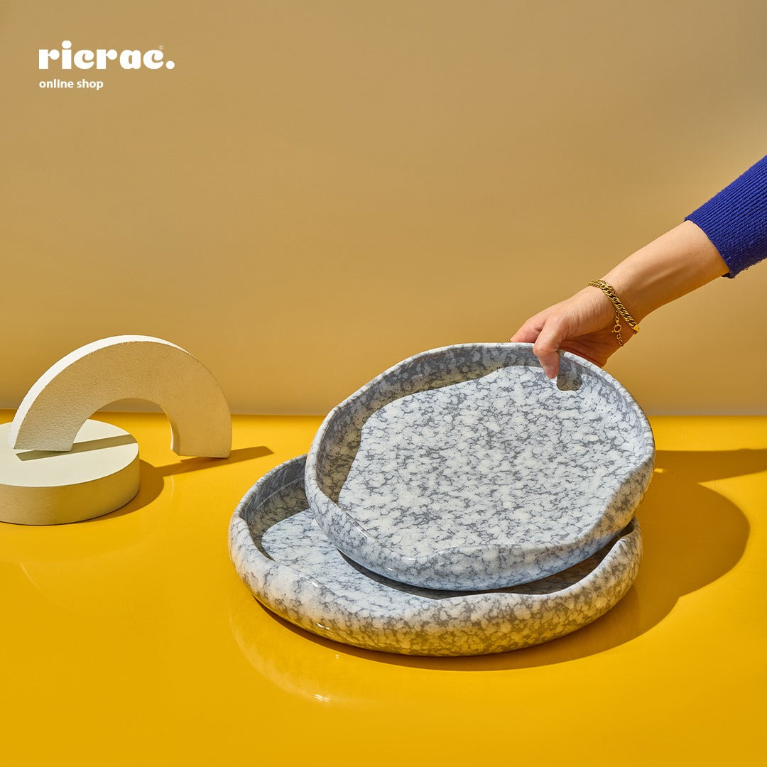 A person holding a unique handcrafted serving plate set in blue and gray tones on a vibrant yellow background.