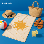 Raya -Microfiber Towel displayed on a beach with a hat, sunglasses, and refreshments, perfect for summer lounging.