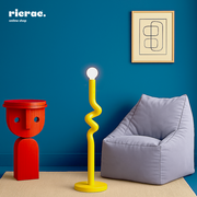Colorful room featuring a yellow metal lighting unit, red sculpture, and a gray bean bag chair against a blue wall.