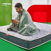 Man sitting on Memory Foam Single Layer Pocket Spring Mattress, wrapped in a blanket, using a smartphone.