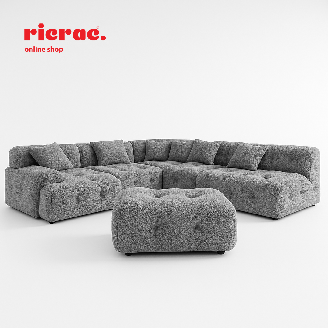 L shape modular sofa in soft grey fabric with tufted cushions and matching puff.