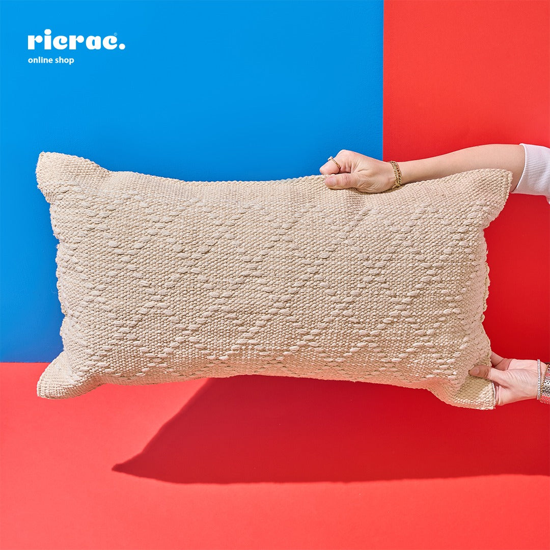 Hand holding a beige bohemian kilim cushion against a bright blue and red background.