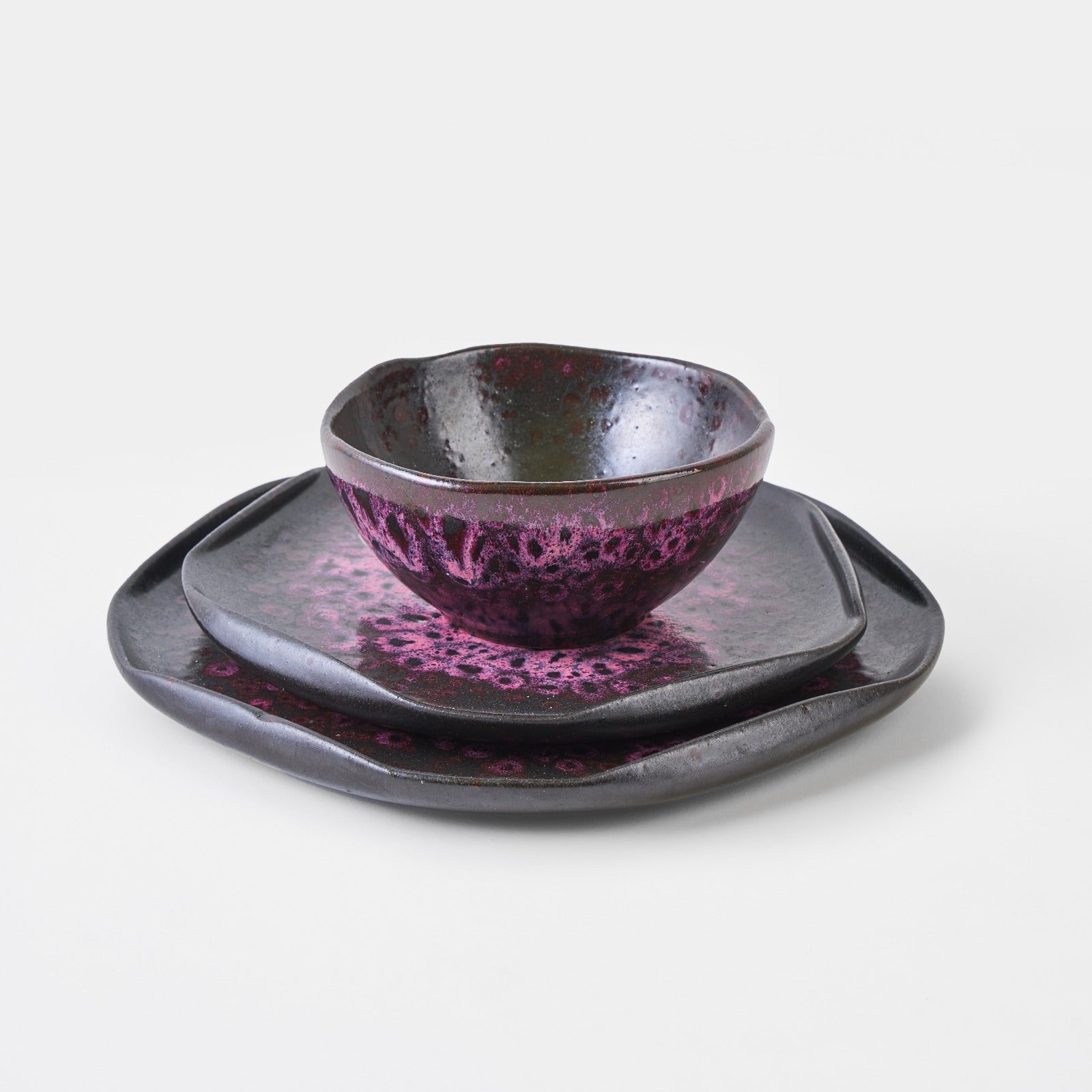 Handmade dinnerware set featuring three plates and a bowl with a unique freckled finish in dark tones.