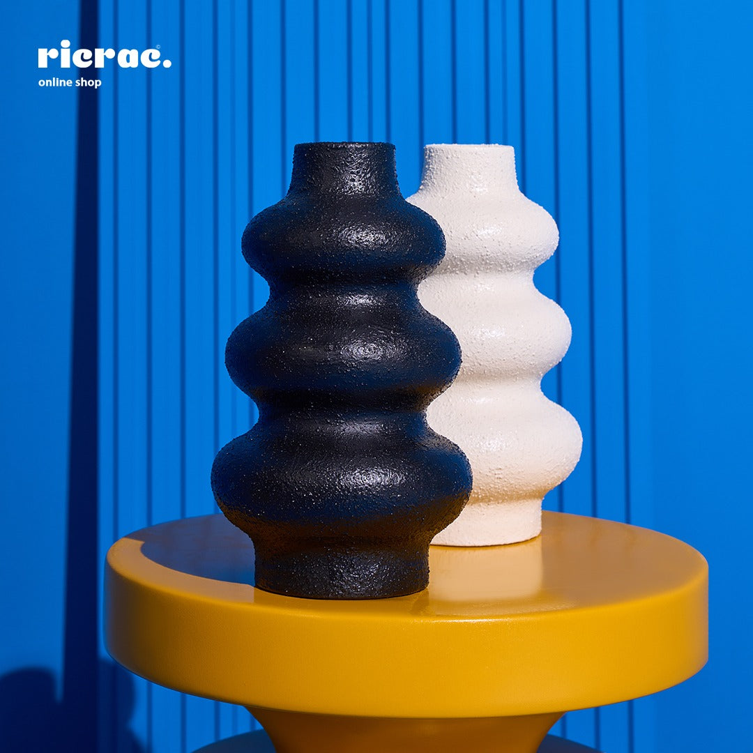 Handcrafted clay accessory vases in black and white on a yellow table against a blue background.