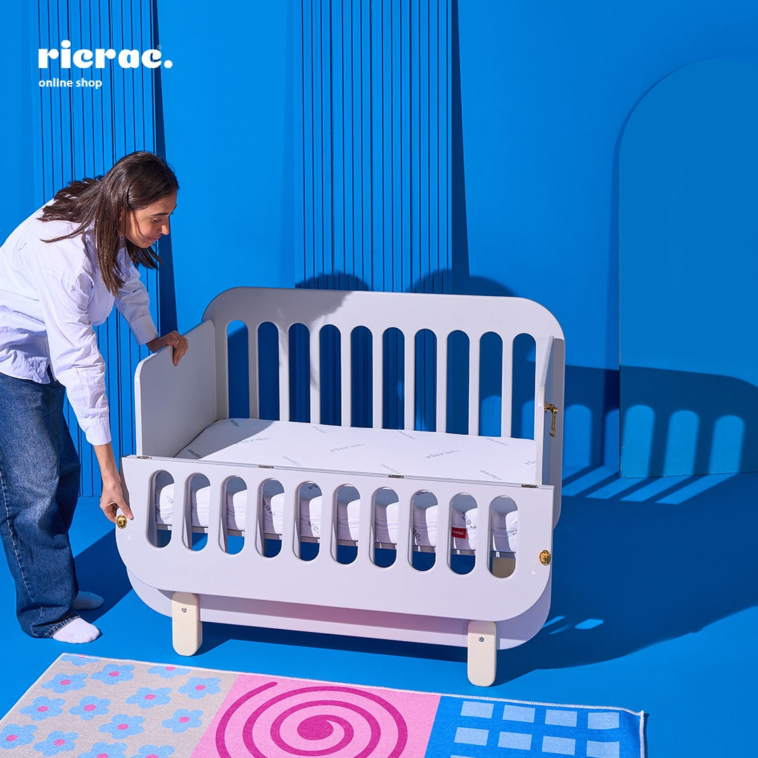 Refook- Baby Cot Bed with a side changing unit in a modern interior setting with vibrant blue background.