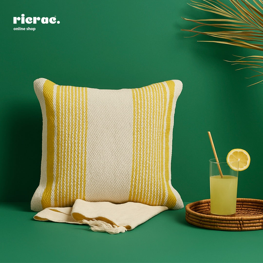 Kilim Cushion- Beige & Mustard Striped on a green background with a drink and accessories.