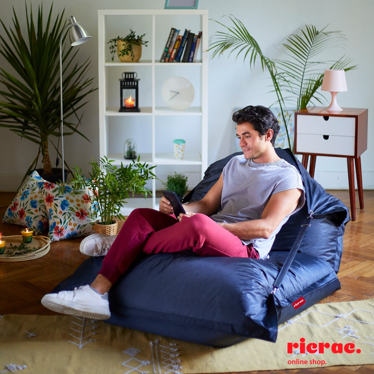 Young man relaxing in Buggle-up Bean bag Lounge Chair, enjoying indoors with plants around, showcasing the bean bag chair's comfort.
