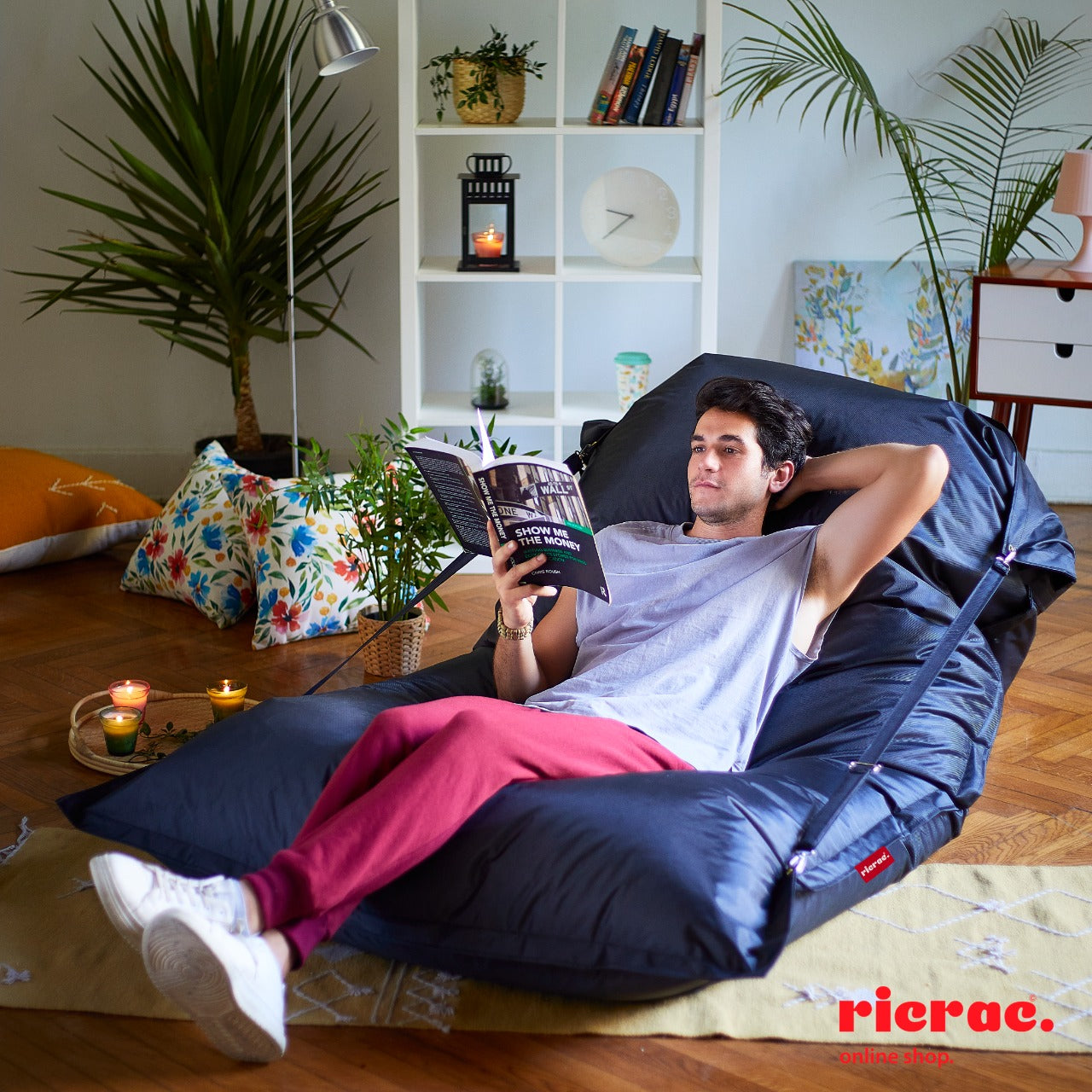 A person relaxing on a Buggle-up bean bag chair indoors, reading a book in a cozy lounge setting.