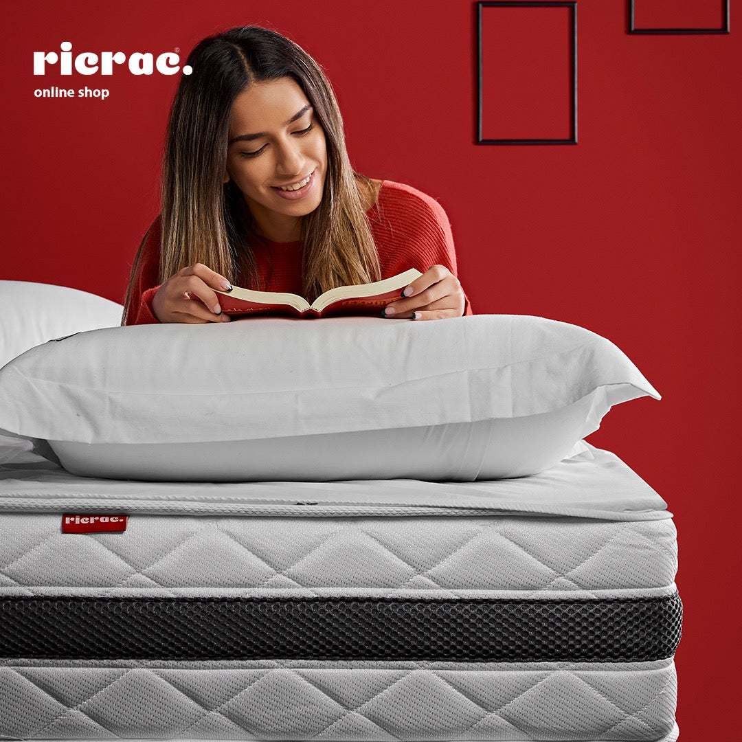 Woman reading on Zoning Mattress- RTS with pillows, showcasing comfort and support in a cozy bedroom setting.